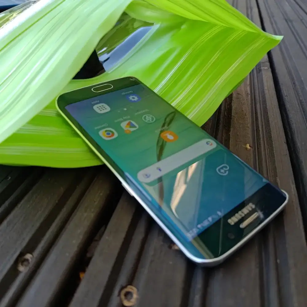 A sleek green samsung galaxy s6 smartphone with curved screen and metallic edges resting on wooden surface for adventure waist pack