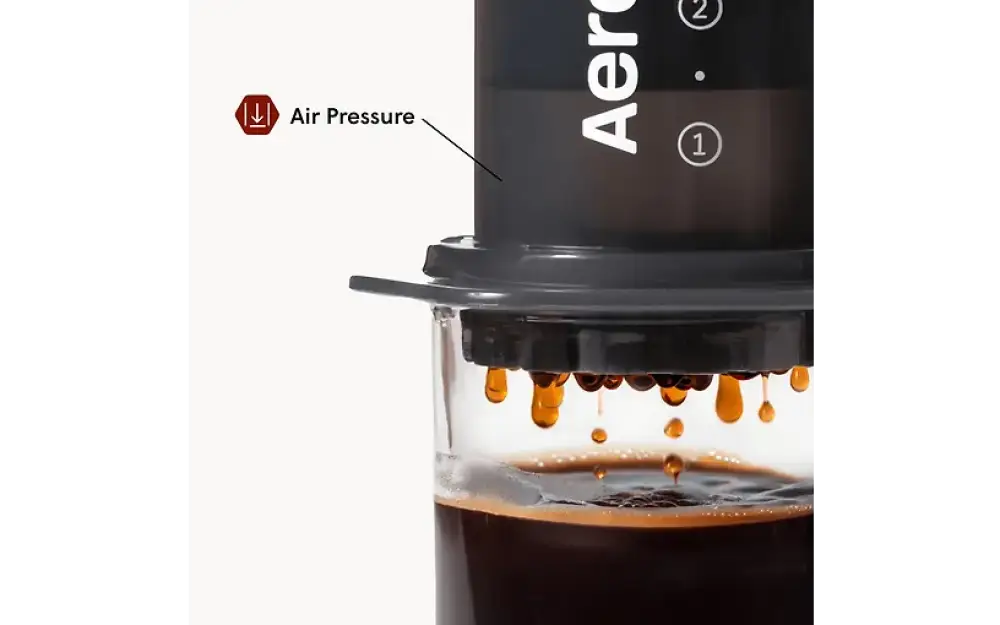 Musta Aerobie AeroPress kahvinvalmistuslaite läpinäkyvällä lasisella pohjalla ja tippuva tumma kahvi