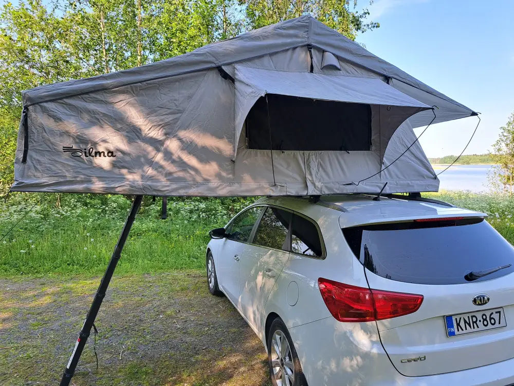 Harmaa kangas autokatossa oleva kattoteltta ilmalla ja mustilla tukipylväillä logolla sivulla