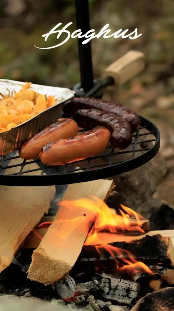 Musta metallinen haghus nuotioteline bbq grilli makkaralla ja foliovuoassa paahdettuja vihanneksia avotulella