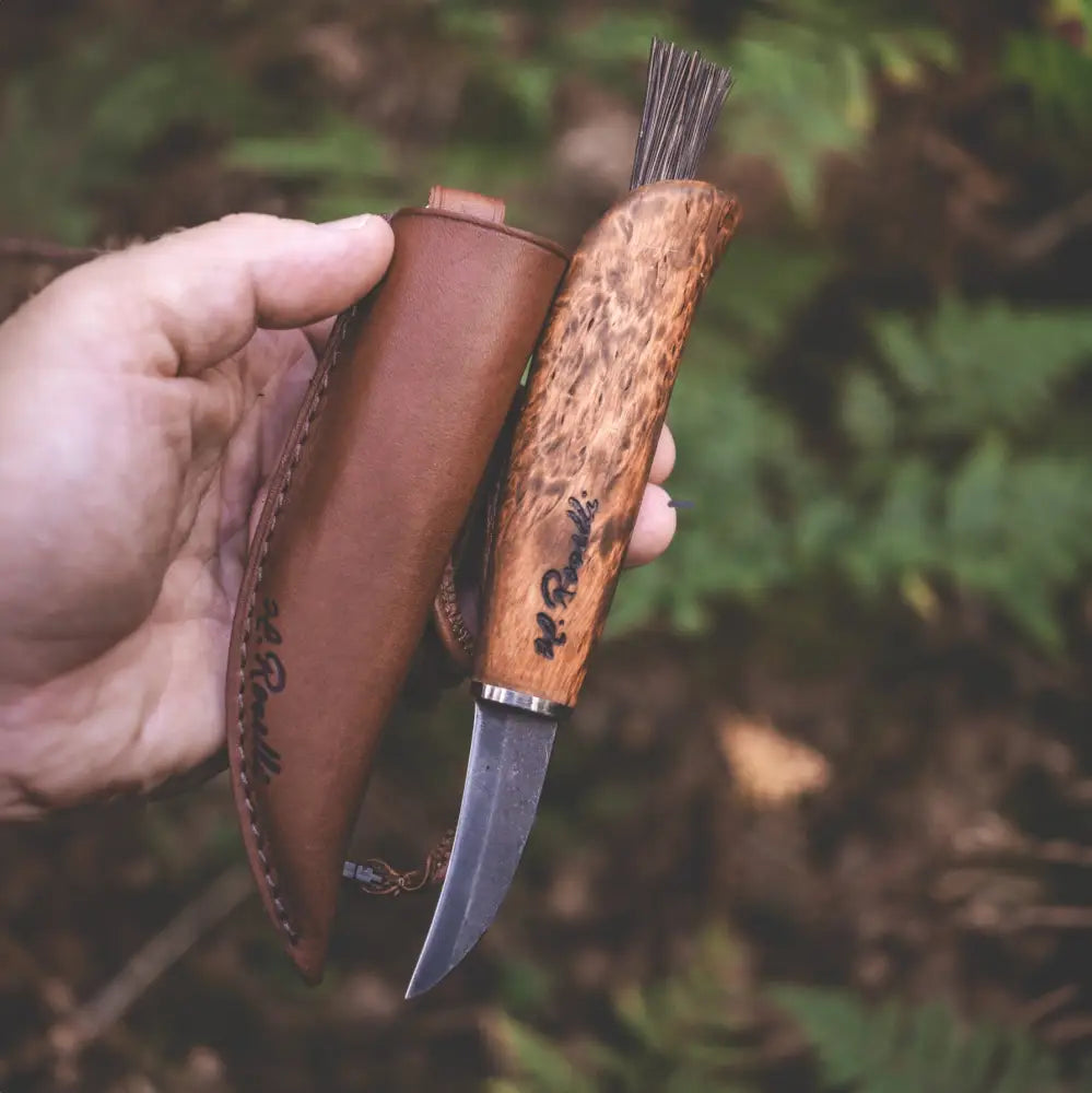 A handcrafted mushroom knife with a curly light brown wooden handle and curved stainless steel blade with leather sheath