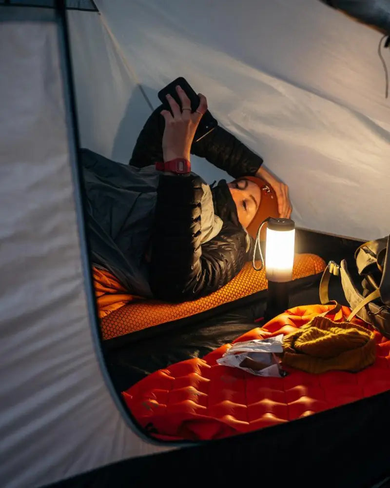 A warm PWR Lantern 300L with a white translucent cylindrical body and black base emits soft light inside a tent
