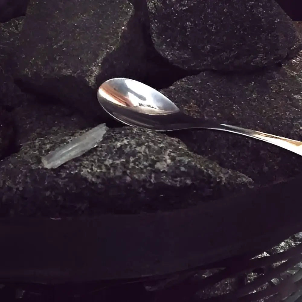 A silver metal spoon resting on dark textured rocks in the relax saunajää product setting