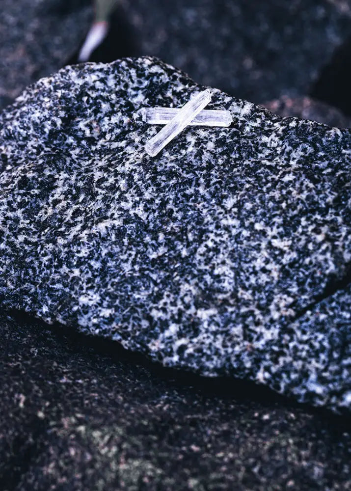 Two translucent crystalline quartz needles form an x on dark gray granite surface in relax saunajää product