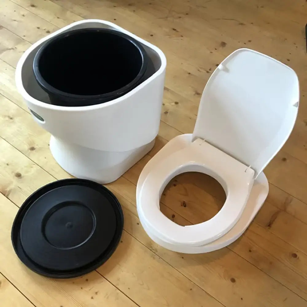 Valkoinen muovinen sanitoa kuivikekäymälä mustalla sisäkammiolla ja kannella etupuolella