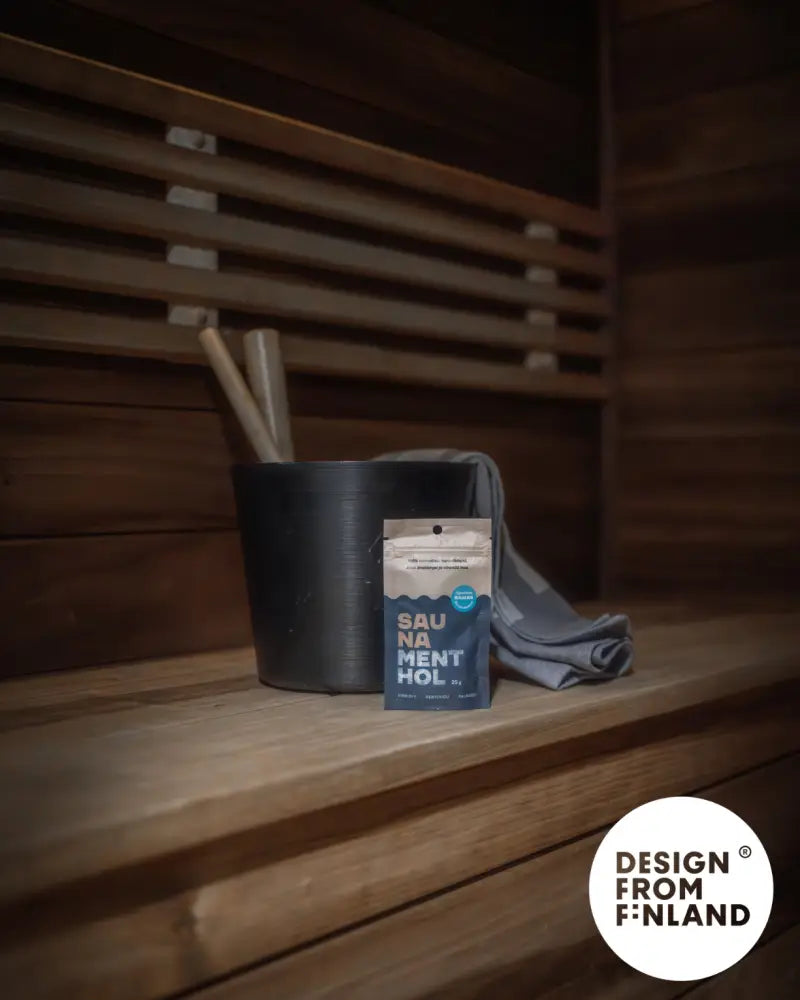 A sleek dark blue pouch of sauna menthol original sauna salt with white and silver label beside black bucket on wooden benches