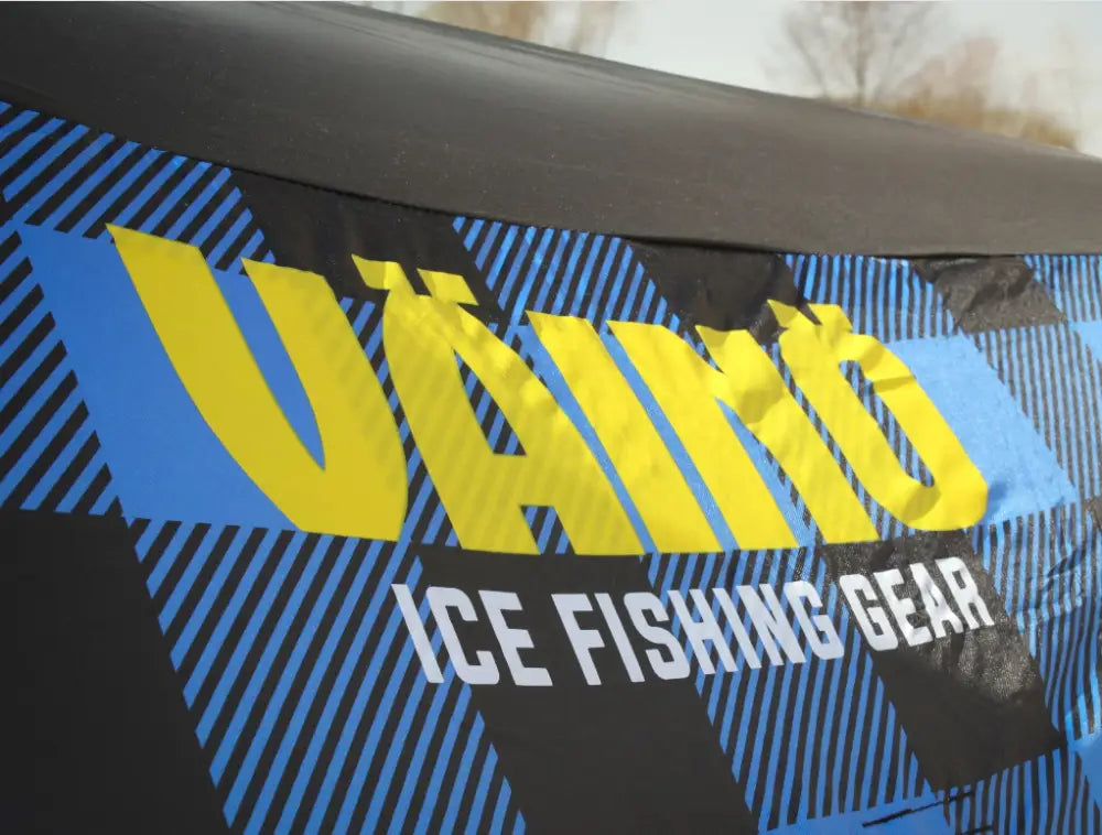 Sinivalkoiset raidalliset väinö bunker 3 glacier edition pilkkiteltta kankaalla, jossa keltainen vänno-teksti ja valkoinen ice fishing gear -teksti