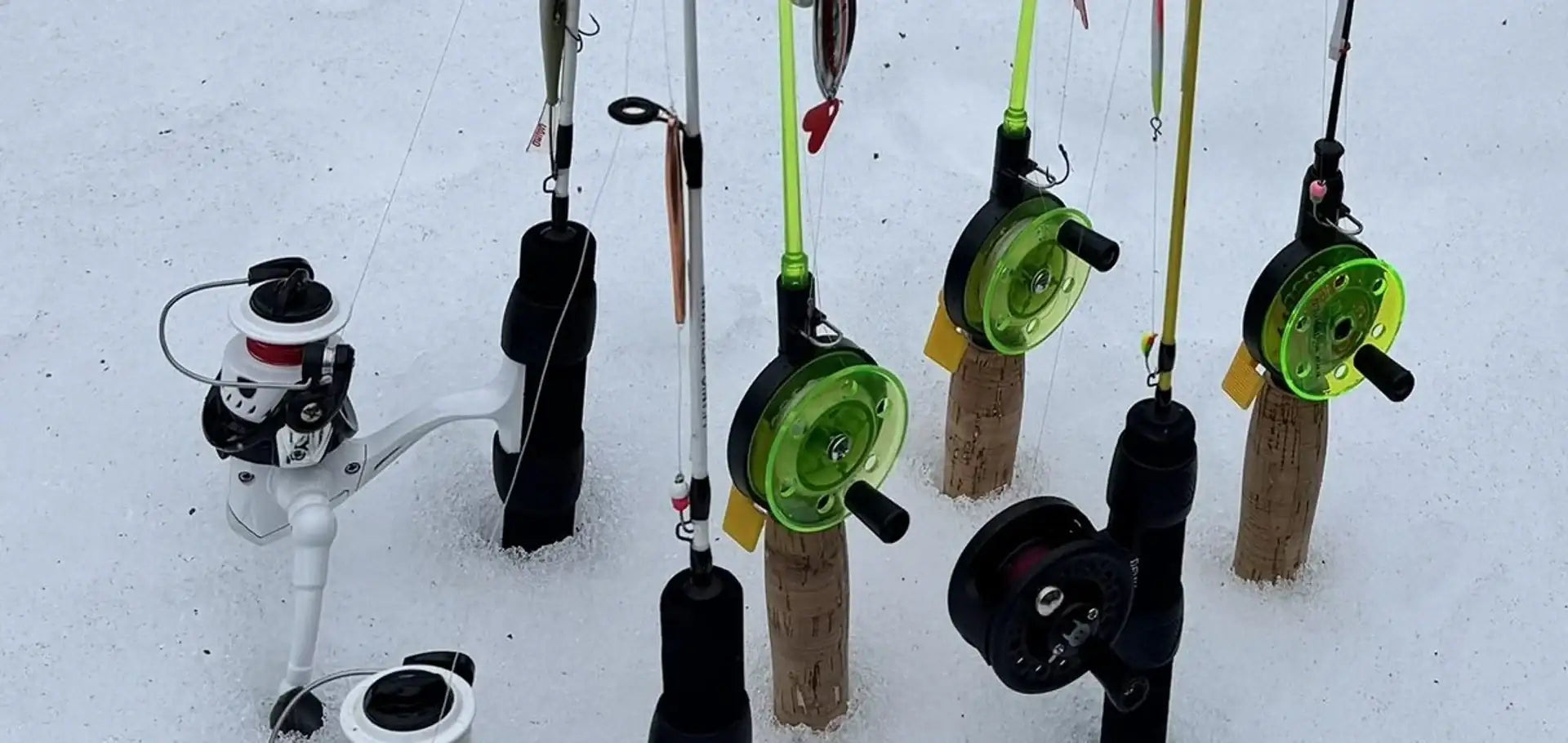 Valkoinen ja musta kalastuskelan, jossa on punainen korostus kahvassa, asennettuna lumipeitteiselle maalle.